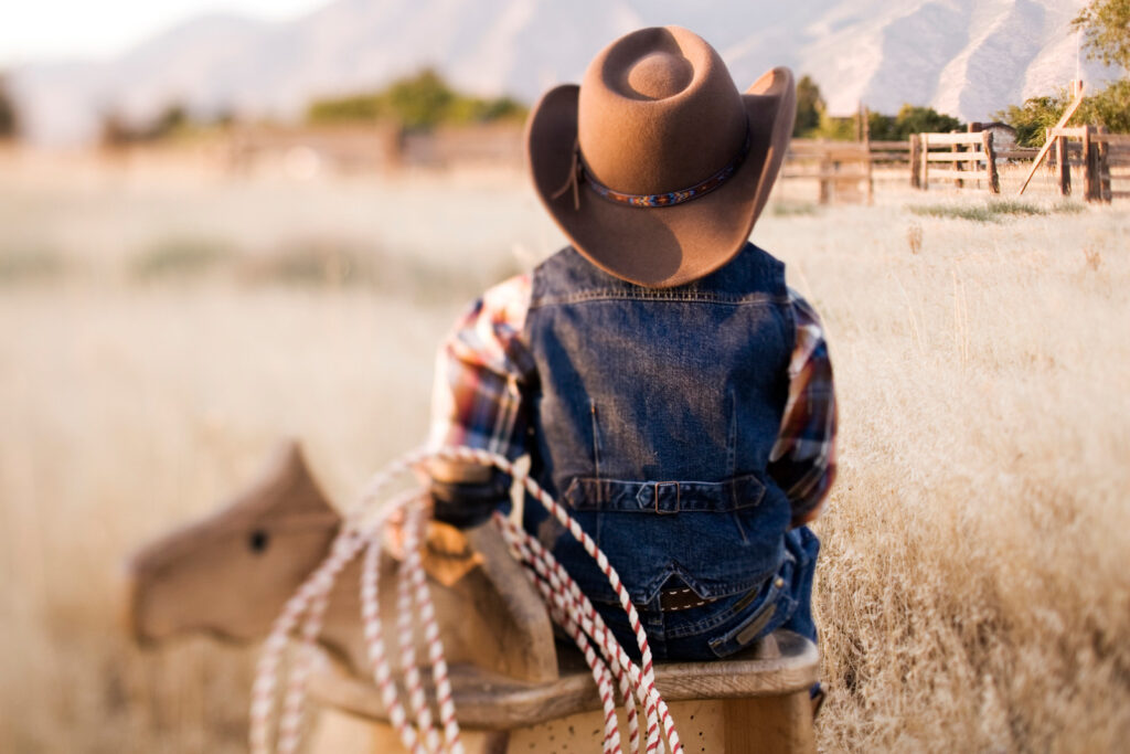 A young cowboy sits on his play horse surveying the ranch.