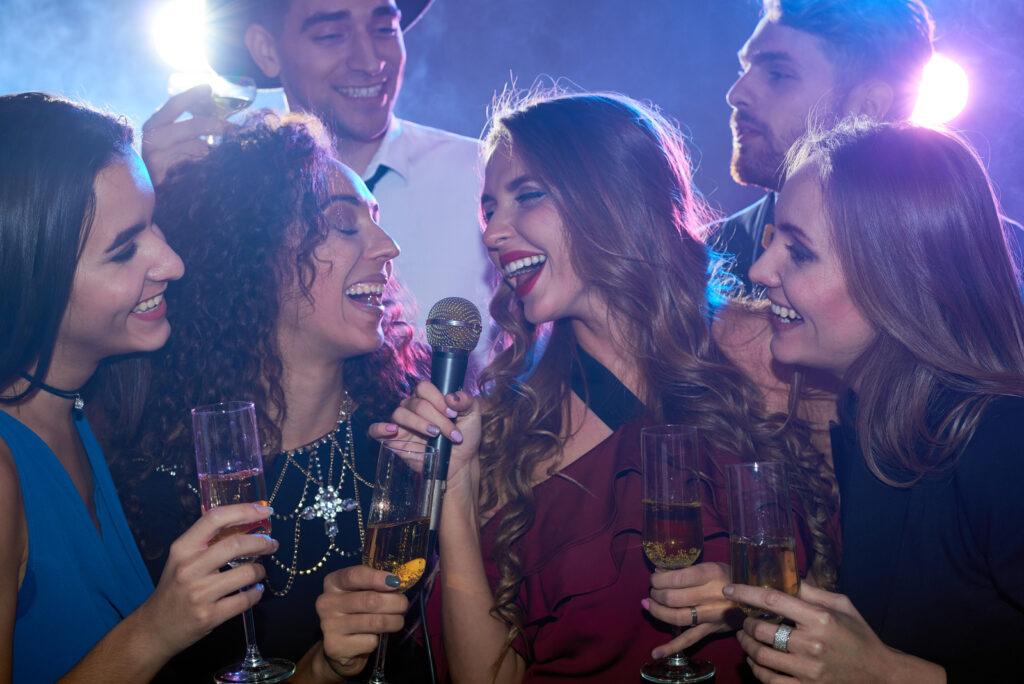 Emotional drunken young women drinking champagne while singing in the karaoke