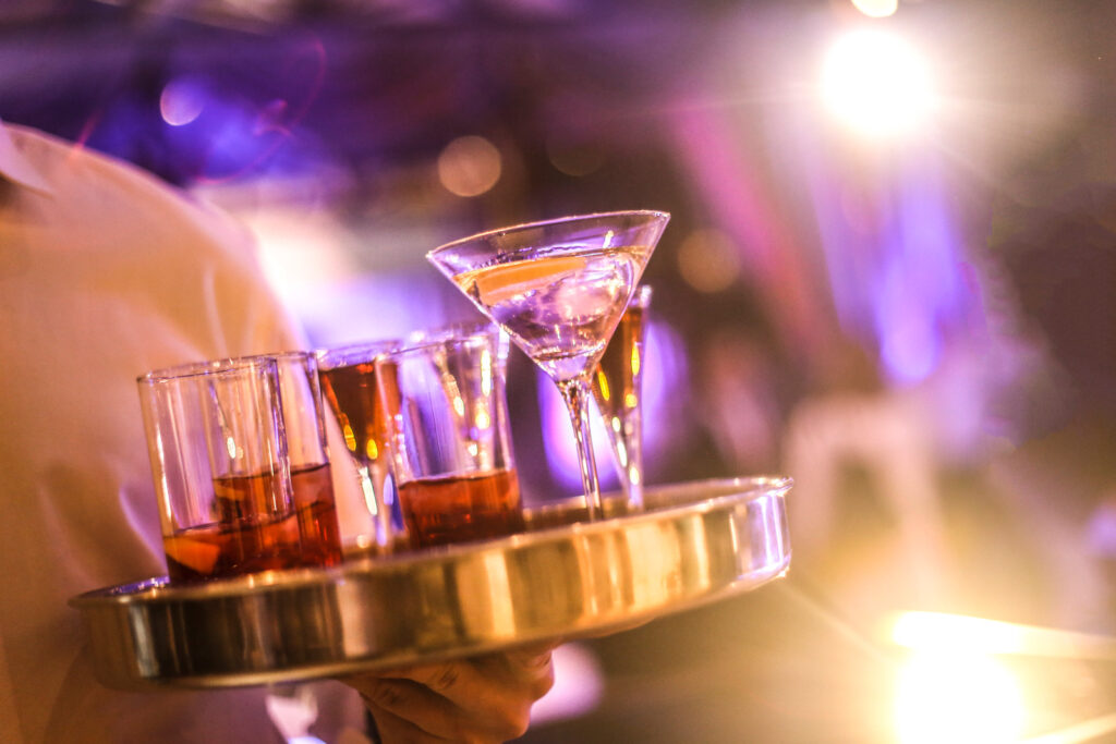 Bartender with serving tray full of various drinks in a nightclub.