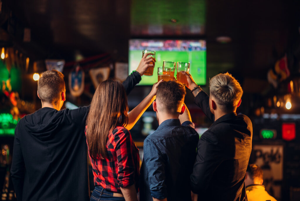 Fun friends watches football on TV and raised their glasses with beer in a sport bar, happy fans, celebration of the victory in game